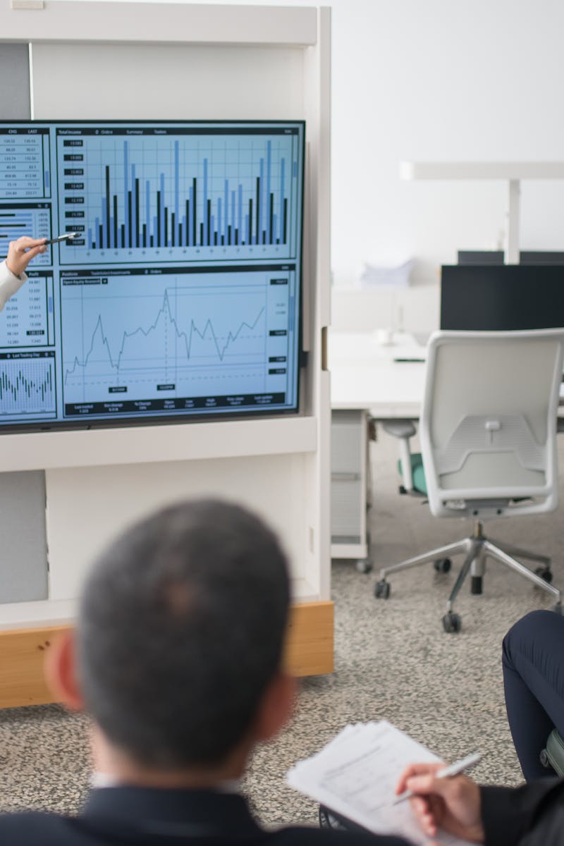 A woman presents data on a screen to a group of colleagues in an open office environment.